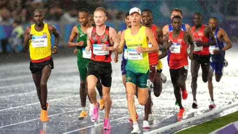 PA The pack of runners, 11 strong, running along the soaking wet track in Glasgow. 