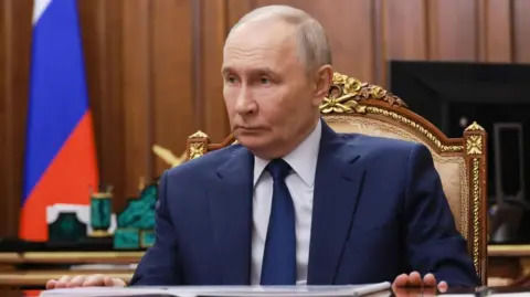 EPA Vladimir Putin sitting on a golden brown chair with his hands resting on a table, while dressed in a navy blue suit and tie.