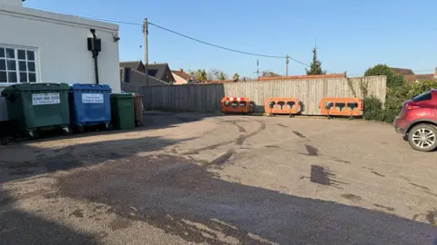 Luke Deal/BBC A view of the pub's rear car park where there are dark stains on the floor where oil has been spilt. Large bins sit at the back of the property and there is a red car parked up. 