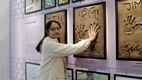 BBC/Suhnwook Lee Jacqueline at a store for BTS fans, touching their palm prints. 