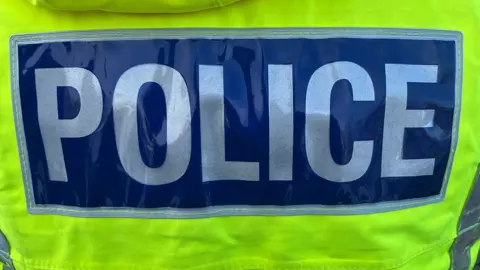 Close up of the words police in white letters on a blue background on the back of a yellow high-visibility jacket