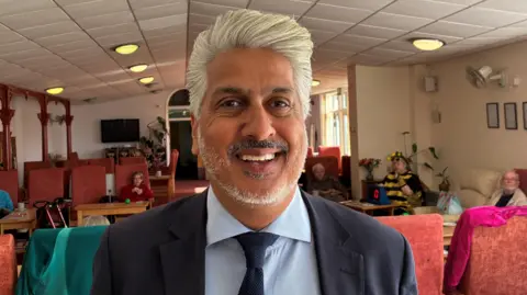 Amerjit Chohan smiles at the camera at a day centre in Penzance and is wearing a blue suit.