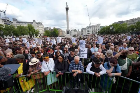 A crowd of people gather in Trafalgar Square as part of a vigil for Jason Arday. Some of them are holding placards.