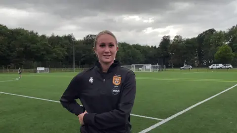 Darcie stands on the pitch in a black Hull City Ladies long sleeved top.
