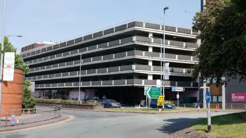 A five-storey car park with white and grey walls and pillars, viewed from a roundabout.