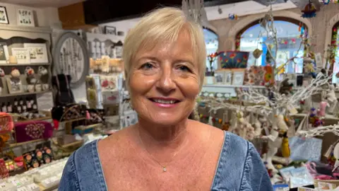 A woman stood smiling with blonde short hair and a denim dress. 