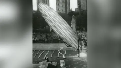 Rochdale Observer A huge structure - the pancake - towering over onlookers is suspended in mid-air being turned. The picture is black and white