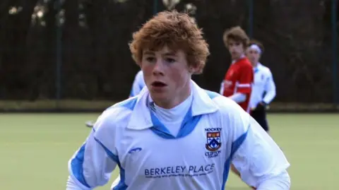 Ryan playing hockey. He is wearing a blue and white hockey kit.