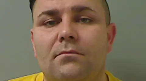 PSNI A police photo of John Scott. He has short, dark hair and is wearing a bright yellow top.