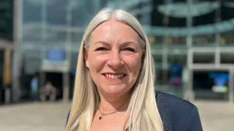 Norfolk County Council leader Kay Mason Billig standing outside The Forum in Norwich, smiling at the camera.