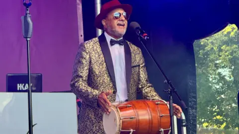 Supplied Surinder with a drum on stage. He is wearing a drum and singing. 