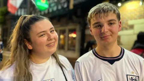 George Carden/BBC A woman and a man standing side-by-side in England shirts.