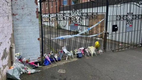 Flowers and police tape outside gates