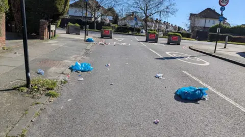 David Ford Rubbish bags can be seen across a road, with rubbish spilling out of them