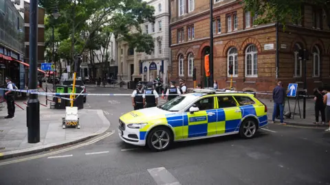 PA Media Police car parked at the end of a London street with a cordon up and officers visible