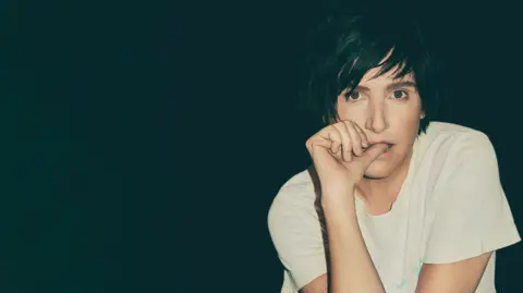 Live at Ludlow Castle Texas lead singer Sharlene Spiteri sat in a white T shirt with her thumb in her mouth and leaning on her elbow - against a black backdrop 