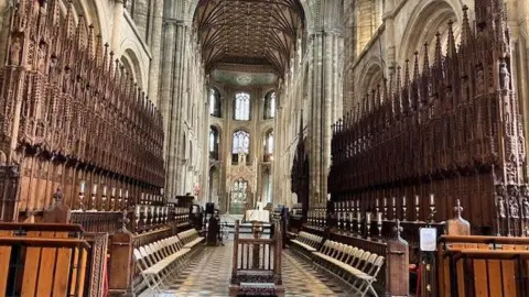 Peterborough Cathedral Inside the cathedral. There are wooden chairs in front of the stalls.