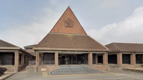 The outside of Guildford Crown Court, showing the steps leading into the building, the steepled roof of red brick and brown tiles.