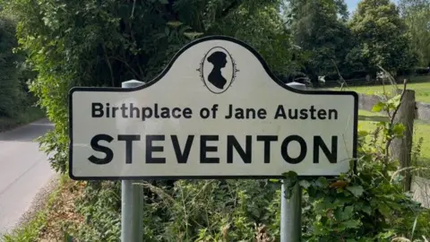 A road sign next to a country lane which reads "Steventon - Birthplace of Jane Austen"