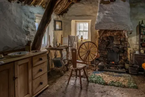 Cruck Cottage Heritage The inside of an old cottage which is kitted out as it would have been many years ago with a fireplace, spinning wheel and other historic items