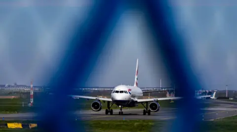 A British Airways airplane is pictured on a railway behind a railing. 
