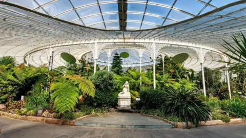 Brian McKenna Interior of the Botanic Gardens in Glasgow, a vast expanse of glass panels over greenery and a statue.