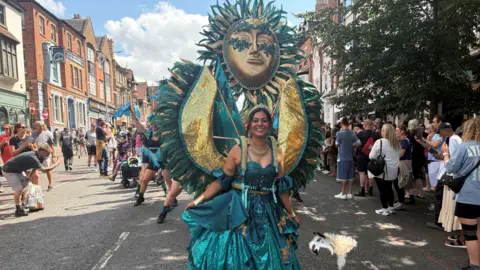 A woman wearing a colourful outfit at the front of a procession of people