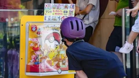 Getty Images A child takes a close look at a Pokemon toy display outside a McDonald's restaurant in Tokyo. He is wearing a blue t-shirt and a purple cycling helmet.