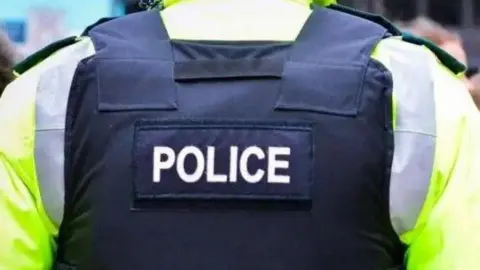 Close shot of a police officers back, wearing a black police vest on a hi-viz jacket