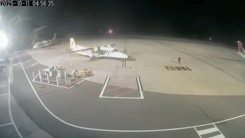 Guernsey Ports A dark image with an Aurigny plane in the foreground and a man matching Russell Payne's description walking towards the camera. 