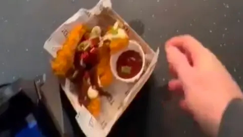 BBC A screenshot of a video of the man picking up a box if chicken tenders from the food counter and walking away without paying