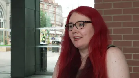A young woman with long bright red hair and black glasses