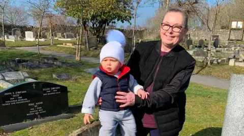 Caroline Sanchez with her grandchild at her mother's grave in Lyndhurst Cemetery 