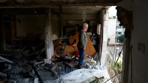 Reuters A man inspects his neighbour's apartment after it was damaged by a rocket fired by Hezbollah, in Kiryat Shmona, northern Israel (20 November 2024)