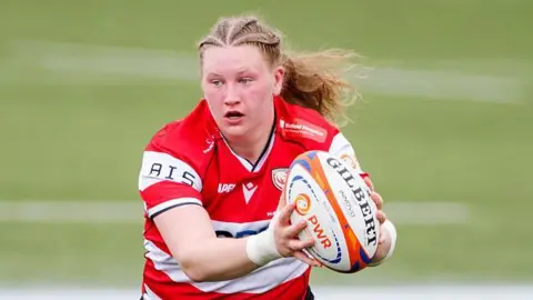 Alaw Pyrs, in action for Gloucester-Hartpury, with the ball out in her hands in front of her body.