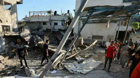 Reuters: People walk through the ruins of a school hit in an airstrike that killed at least 16 people.