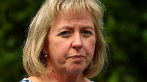 A close-up of Catherine O'Sullivan. She is looking directly at the camera and has short blonde hair with a fringe. 