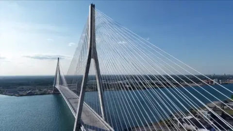 An aerial view of a long bridge connecting the US and Canada, with blue skies and water.