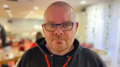 A bald man with black glasses.
