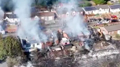 Drone shot from high above smouldering building in a terraced street as smoke rises into the air