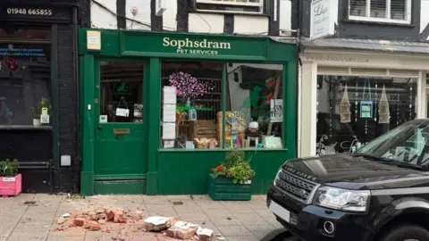 Glenn Jenkinson-Deakin Rubble lies on the pavement outside a green painted shop frontage with Sophsdram Pet Services written above the window. A black Land Rover can be seen parked alongside it, and other ships either side, including a beauty salon.