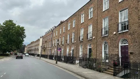 A row of Georgian-style brick townhouses with metal railings outside, and steps up to their front doors.