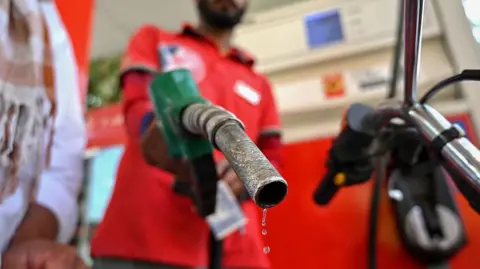 An attendant at a petrol station refills a motorbike with fuel