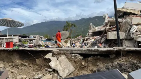 Kent Fire and Rescue Service A man in an orange hi-vis jacket standing on top of a collapsed building.