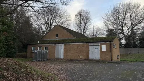 Outside the Deddington Exchange on an overcast day. There is a bicycle rack beside the building with four bikes.