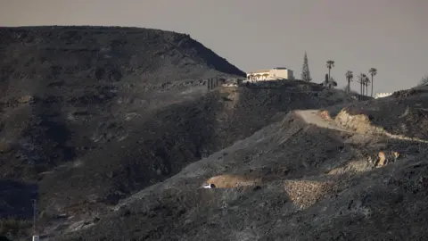 Burnt hills and a single house in the distance after wildfires through Almeria province, Spain.