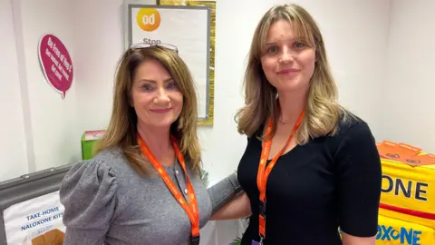 BBC/Richard Edwards Sam Thomson and Sarah Rogers from North Yorkshire Horizons look straight towards the camera. Sam is wearing a grey top, Sarah is wearing a black top. They have orange lanyards around their necks.