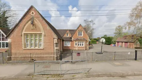 The outside of a school building with a playground and basketball hoops outside. There is also a black railing around the school.