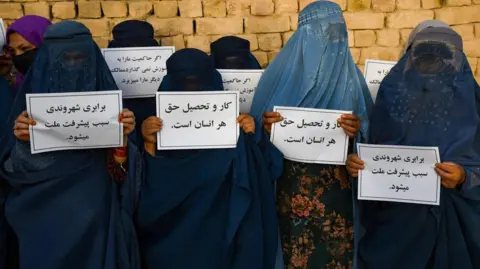 2023 年 8 月 12 日，在马扎里沙里夫，身着罩袍的阿富汗妇女举着标语牌抗议，争取受教育的权利。 (