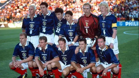 Getty Images Scotland men's team lined up, wearing dark blue shirts, white shorts and red socks at the 1998 World Cup.